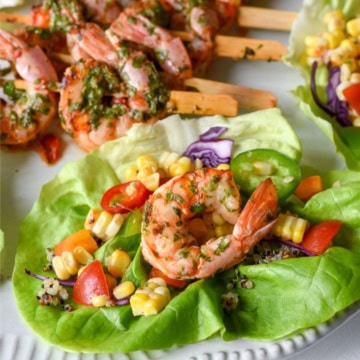 A close-up of a shrimp lettuce wrap with a corn salsa and shrimp skewers in the background.