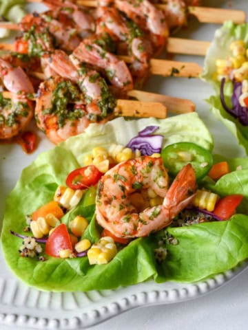 A close-up of a shrimp lettuce wrap with a corn salsa and shrimp skewers in the background.