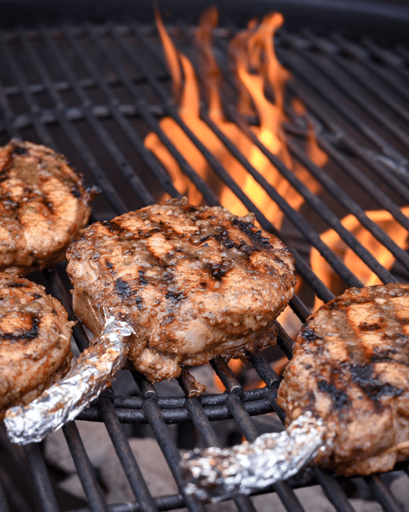 Pork chops on a flaming grill. Frenched bones are covered with aluminum foil. 