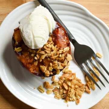 A grilled peach with a crumble topping and a scoop of vanilla ice cream.