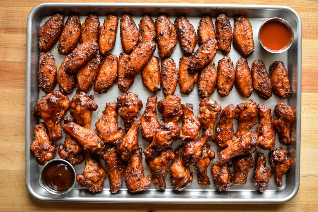 A sheet pan filled lined with chicken wings and two dips. 