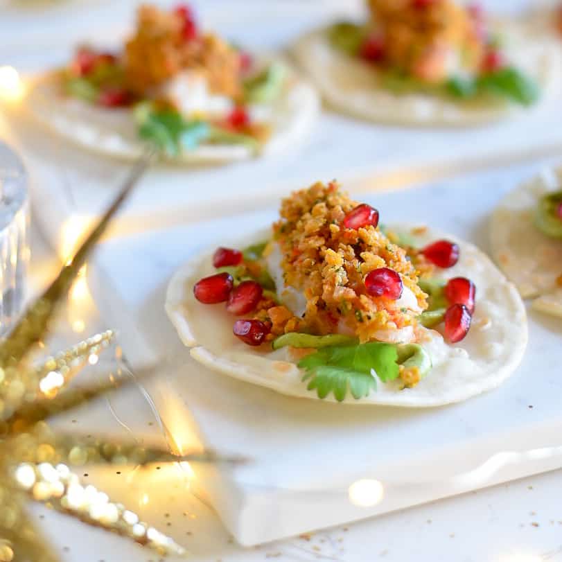 A close up of a baked shrimp appetizer bite with pomegranate arils.