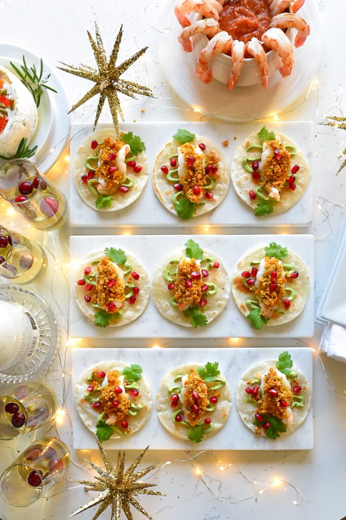 A festive table setting with nine shrimp tortilla bites appetizers and a bowl of shrimp cocktail. 