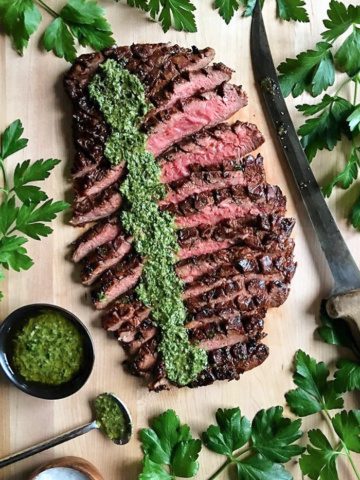 A balsamic marinated flank steak sliced thinly with a row of chimichurri sauce poured down the side.