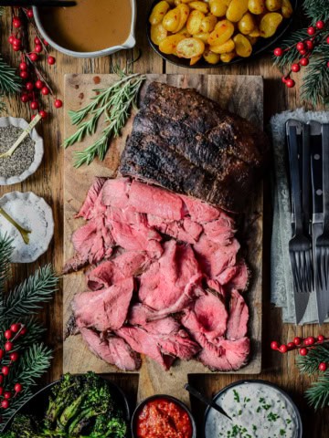 A grilled roast beef with half of it sliced thinly to reveal a perfect medium rare cook. Served with gravy, bomba potatoes and a horseradish cream sauce.