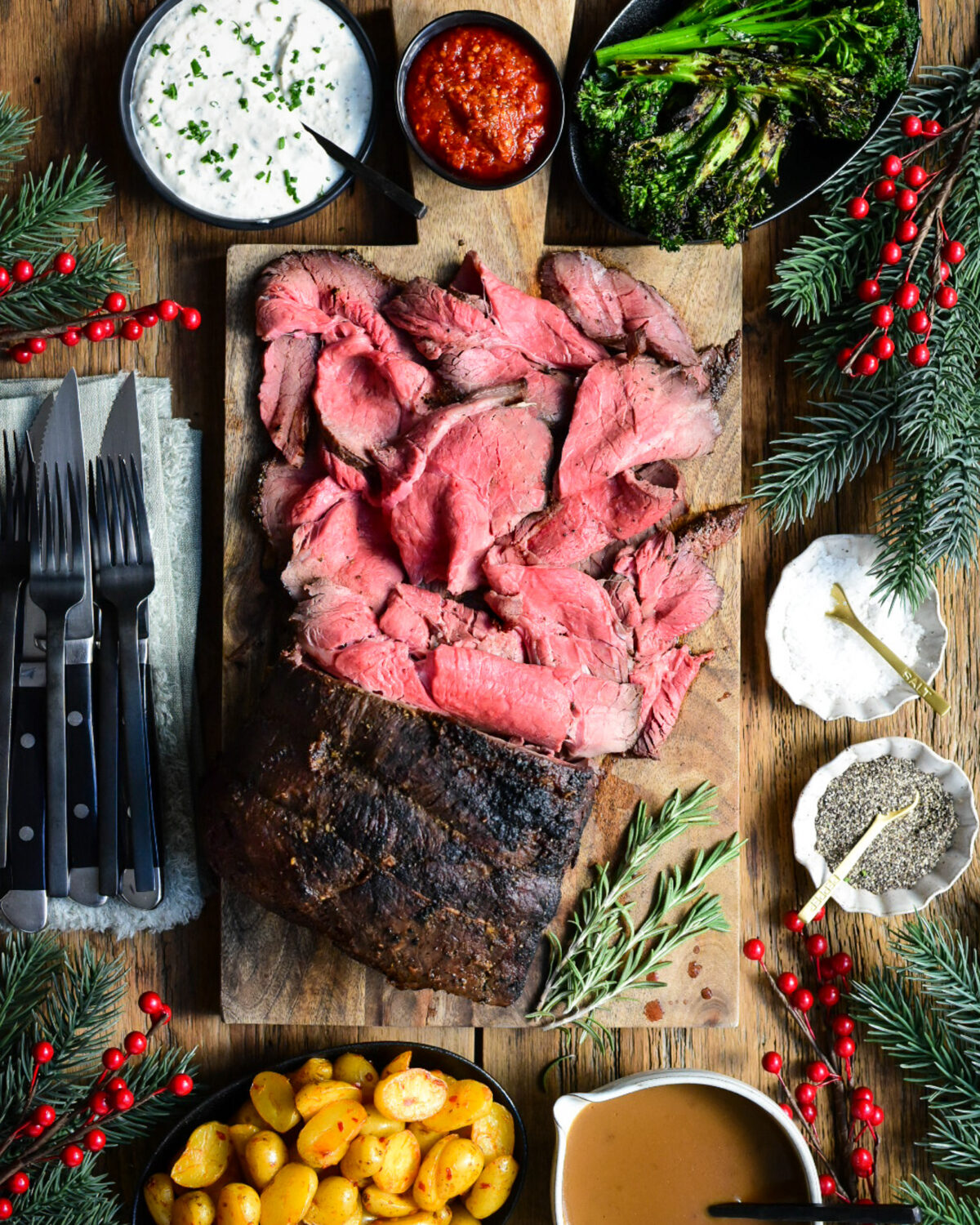 A large medium rare roast beef on a cutting board. Half of the roast is sliced into thin pieces. Served with gravy, potatoes, horseradish sauce and broccolini.