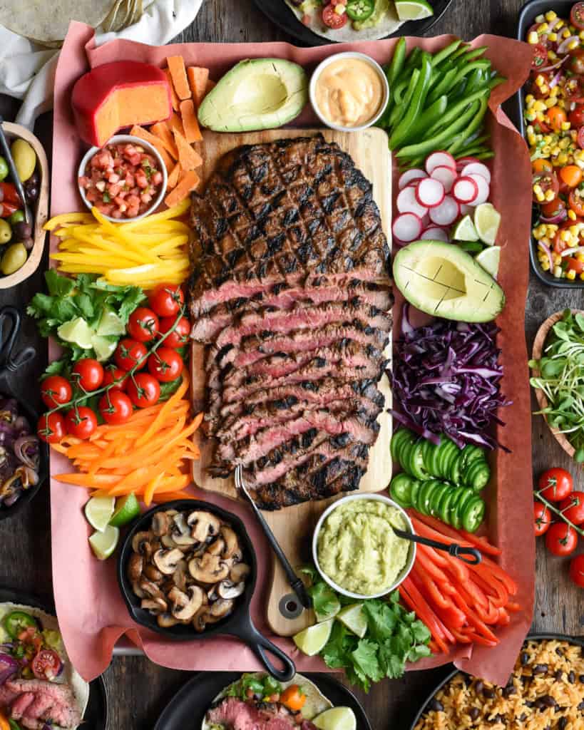 A spread of a sliced flank steak surrounded by an abundance of colourful toppings.