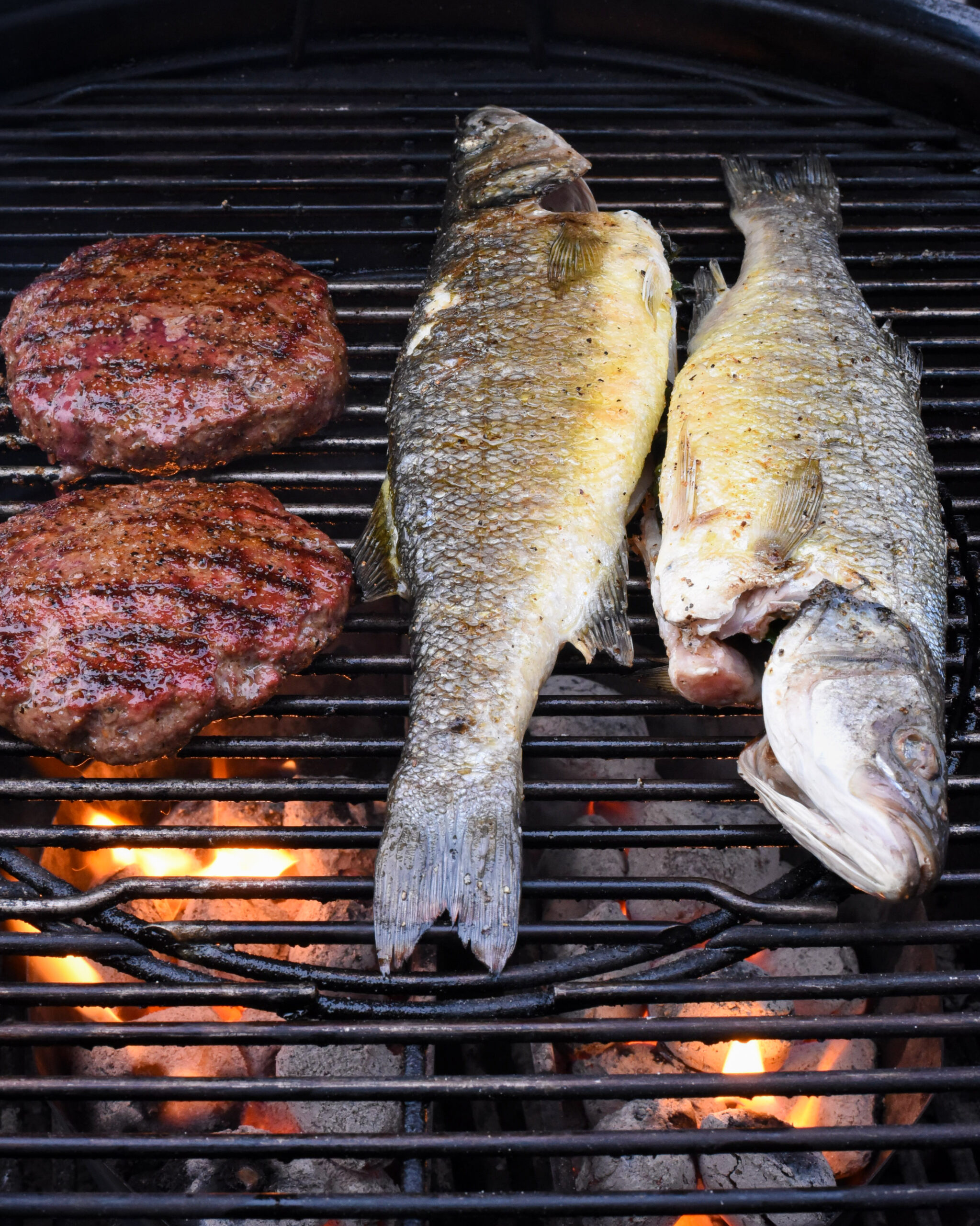 Two whole fish and two burgers on the grill.