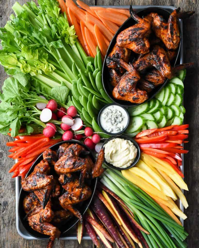 A large platter of chicken wings and a variety of vegetables and dip.