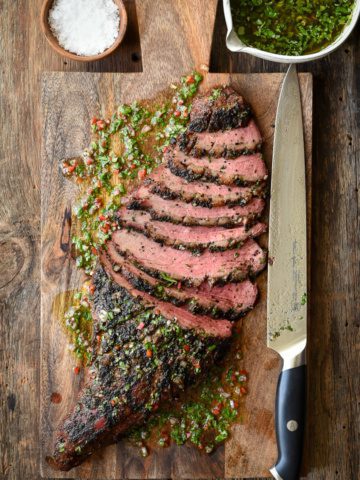 A sliced Grilled Tri-Tip with Chimichurri on a board with a carving knife.