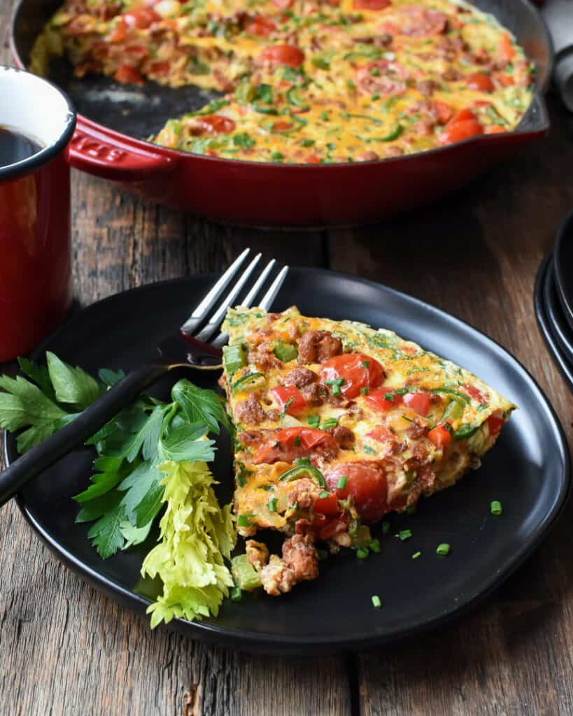 A slice of hot Italian sausage frittata on a plate in front of the skillet. 