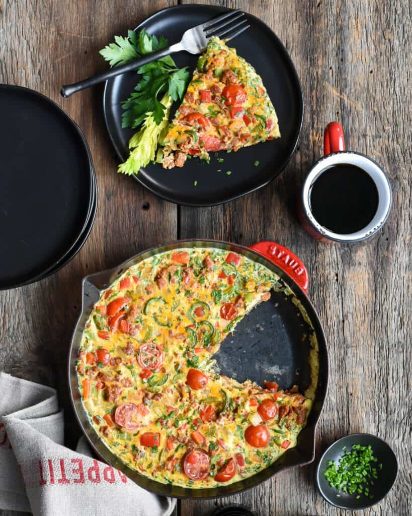 A Hot Italian Sausage Frittata in a skillet with a wedge cut out on a plate. 