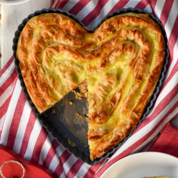 A Sausage and Feta Phyllo Pie rolled in coils and baked in a heart shaped pan. A slice is missing.