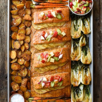 Four portions of salmon on a cedar plank, served with apples, bok choy and potatoes.