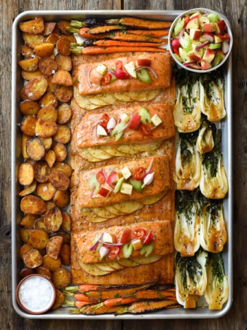 Four portions of salmon on a cedar plank, served with apples, bok choy and potatoes.