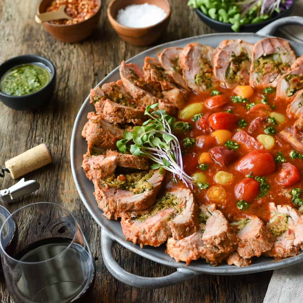 Round platter with a slices of stuffed pork tenderloin with a tomato base in the center. 