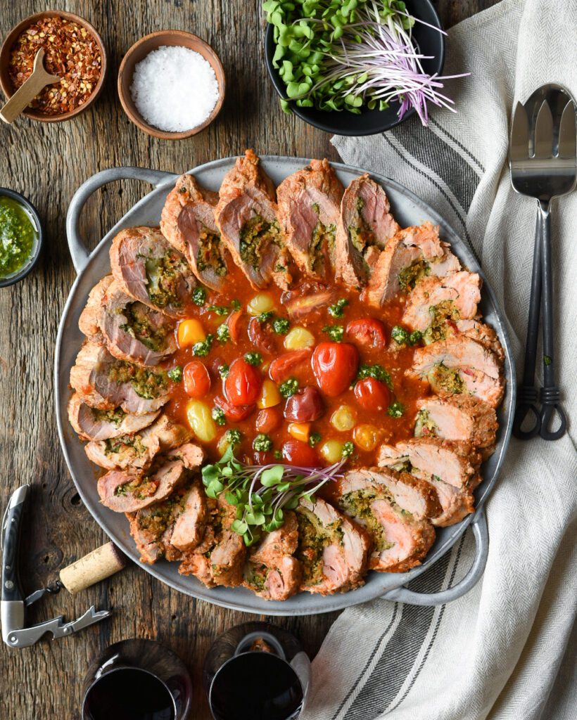 Round platter with a slices of stuffed pork tenderloin with a tomato base in the center. 