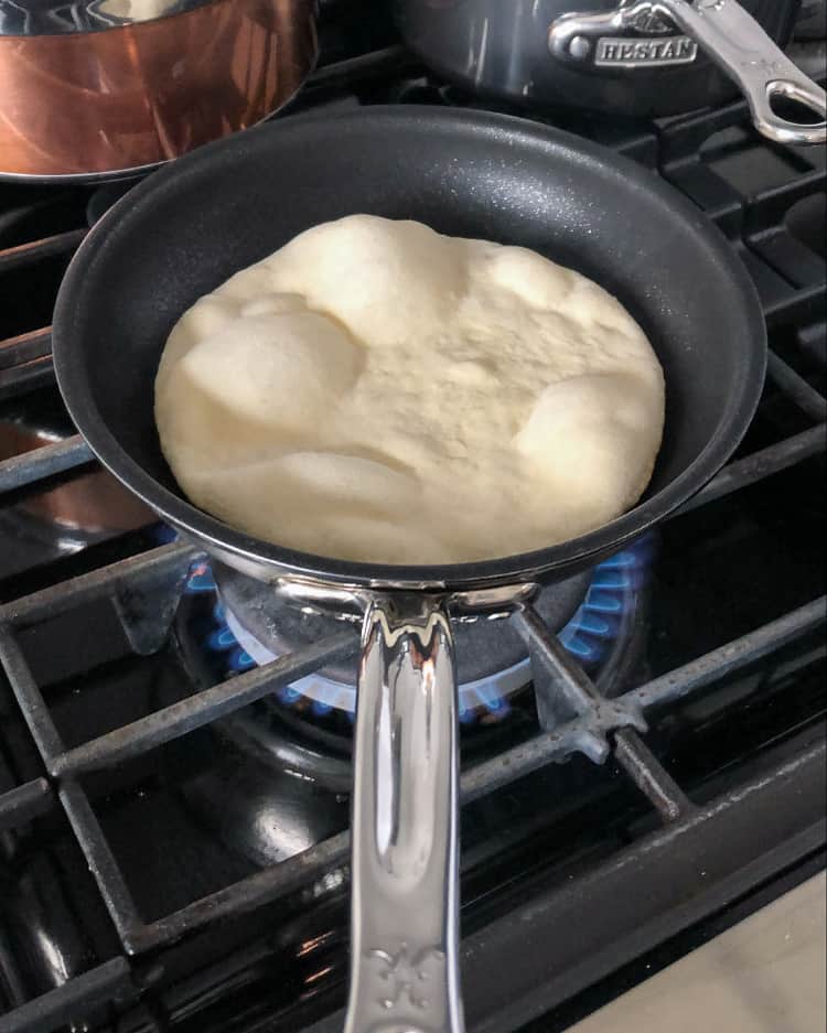 A flatbread (naan) being made in a skillet on the stove top.