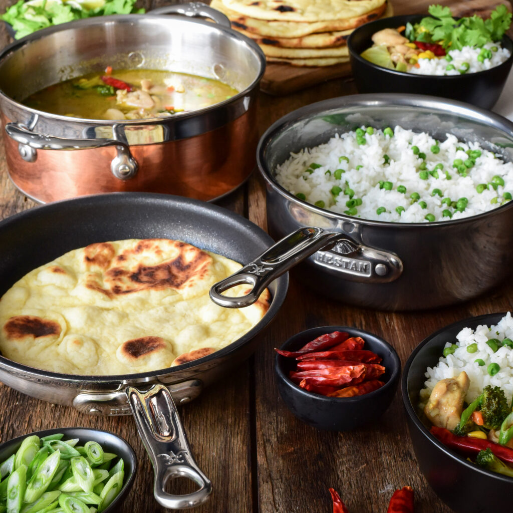 An image of a pot of Thai green curry chicken, a pot of rice and peas, a pan with flatbread (naan) and two bowls with a mixture of everthing.