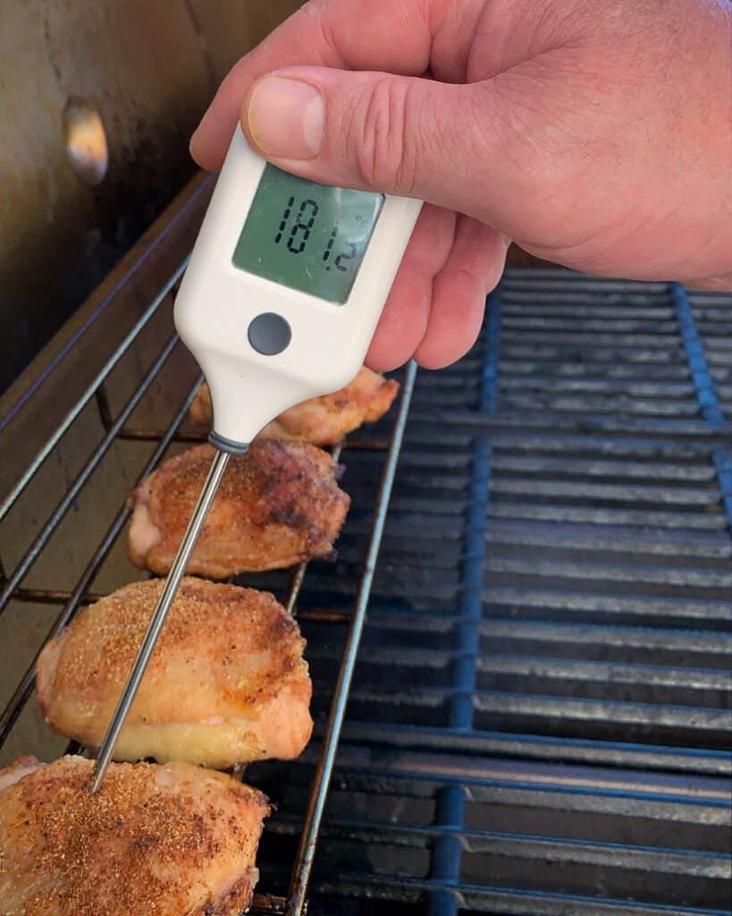 An image of chicken thighs on the grill with a thermometer showing the tempurature of 181 degrees.