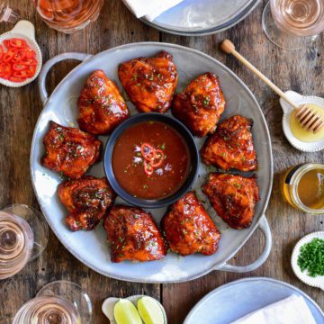 A round platter of Sweet-Heat Grilled Chicken Thighs served with a bowl of sauce.