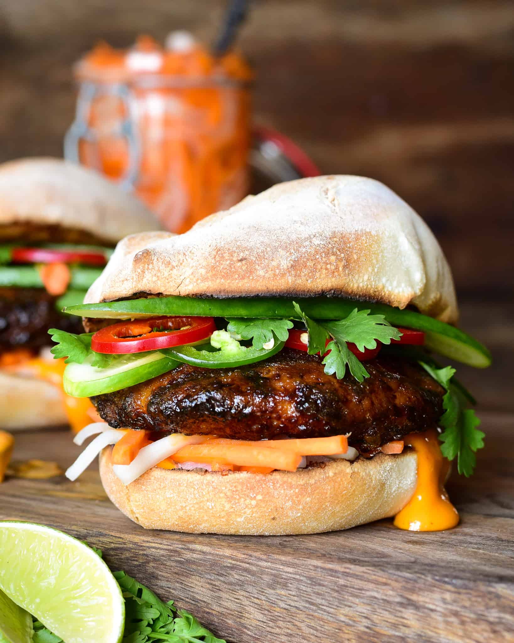 A side view of a Bánh Mì pork burger loaded with pickled and fresh vegetables and sauce on a French roll.