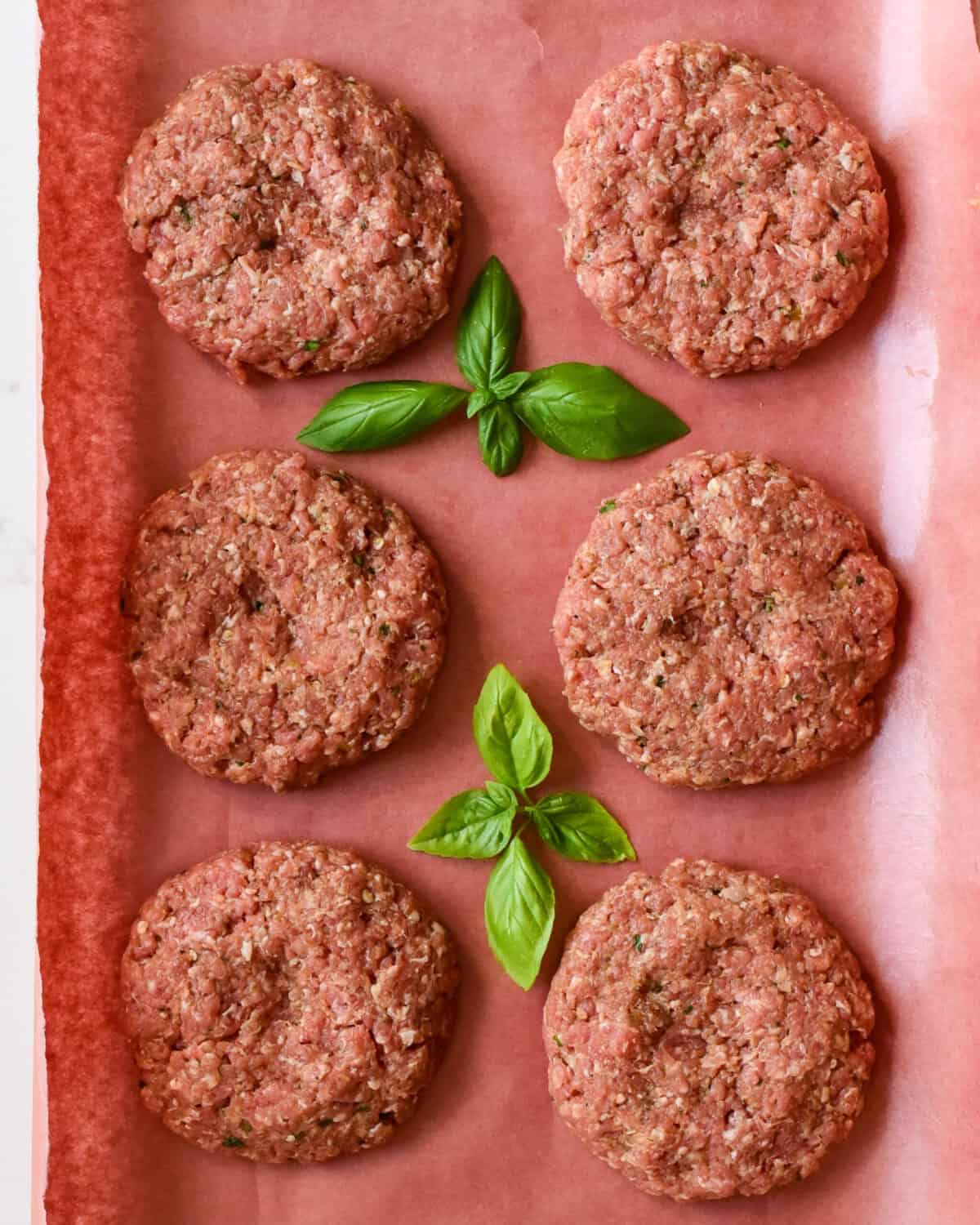 Six pork patties with indents in the middle to keep the burgers from puffing up when cooked. Basil leaves in between the patties.
