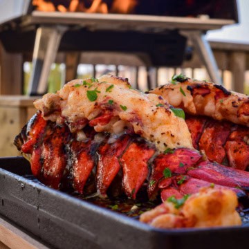Two lobster tails on a cast iron skillet in the Ooni Koda 16 oven.