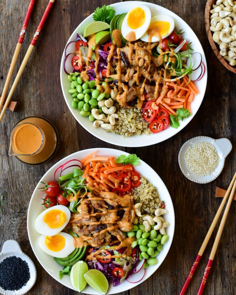 Two colourful chicken grain bowls with peanut sauce, boiled eggs and veggies.