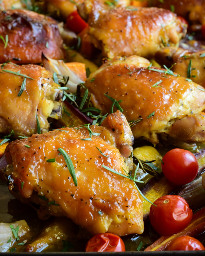 Close up photo of  a sheet pan of chicken thights with rosemary, taragon and veggies.