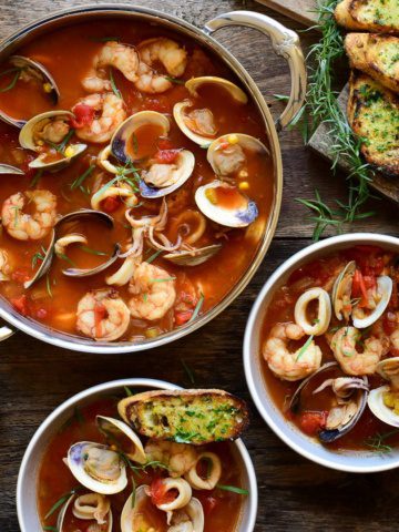A soup pot and two bowls filled with a seafood and a side of garlic butter toast.