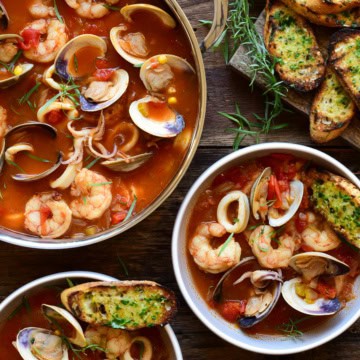A soup pot and two bowls filled with seafood and a side of garlic butter toast.