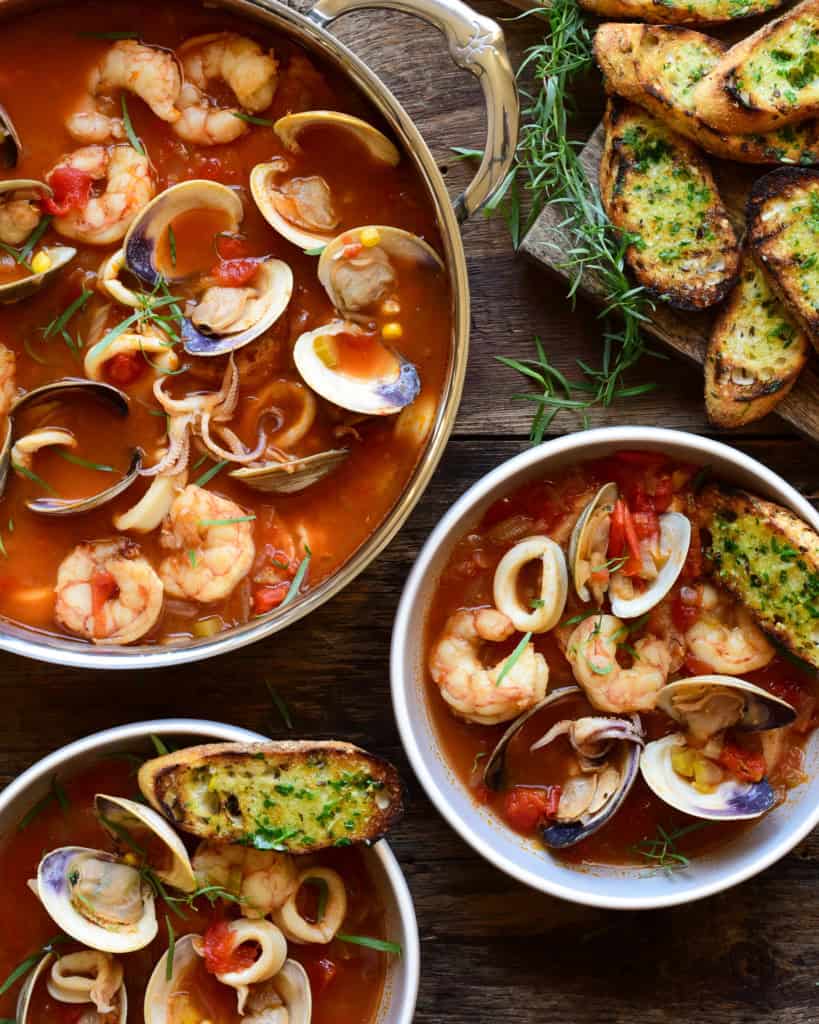 A soup pot and two bowls filled with seafood and a side of garlic butter toast.