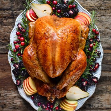 A moist and juicy roasted turkey perfectly golden on a platter decorated with fruit.