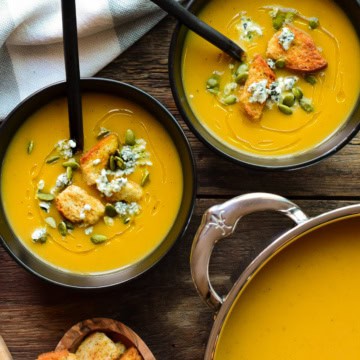 Two bowls and a pot of puréed roasted vegetable soup.