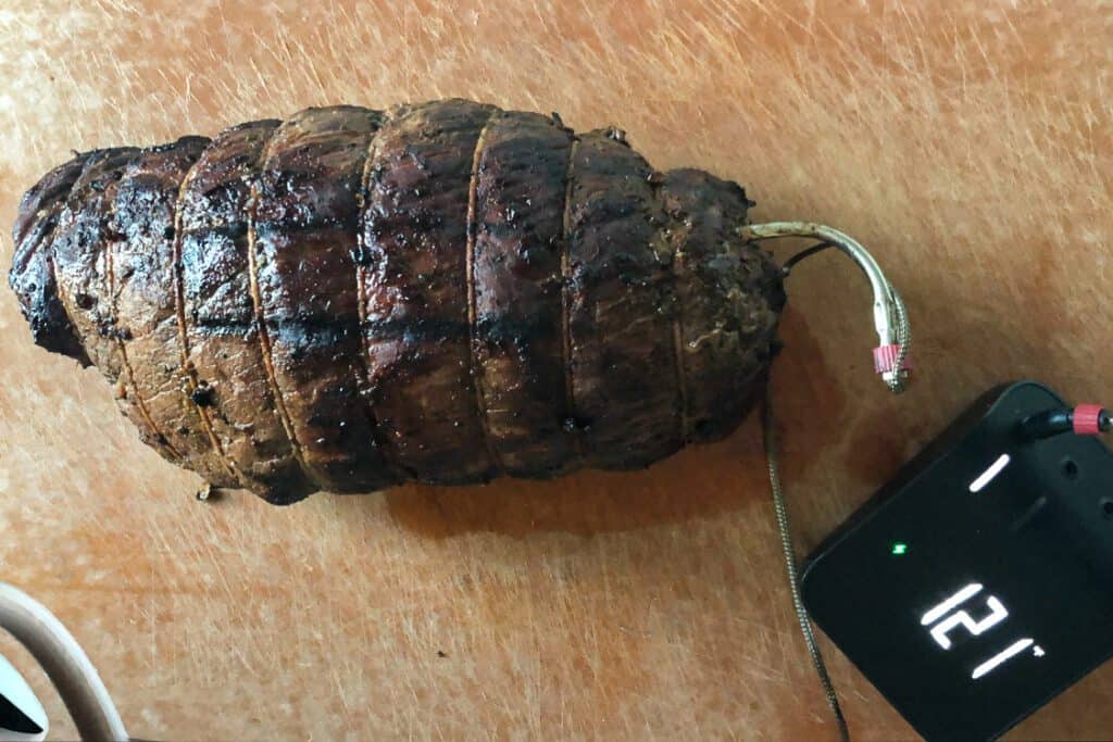 A rested image of grilled roast with a temperature probe reading 121 °F and ready to carve. 