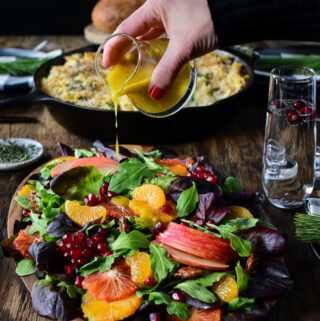 Drizzling salad dressing over a colourful Winter Citrus & Baby Green Salad