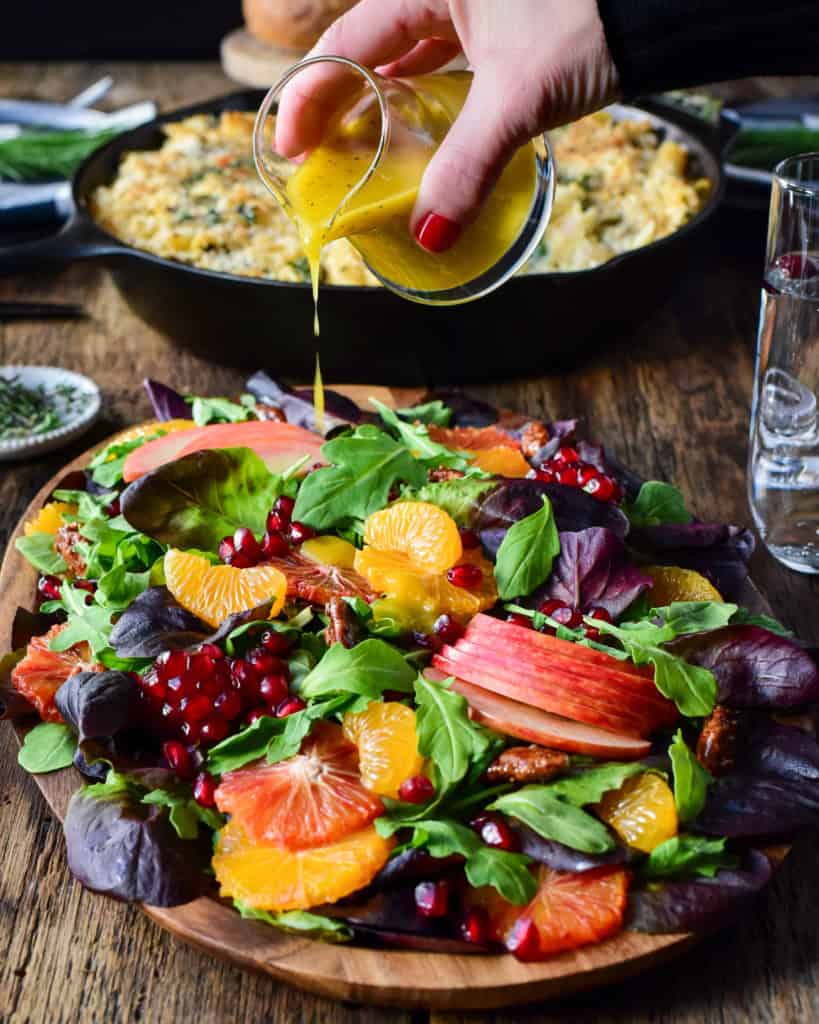 Drizzling salad dressing over a colourful Winter Citrus & Baby Green Salad