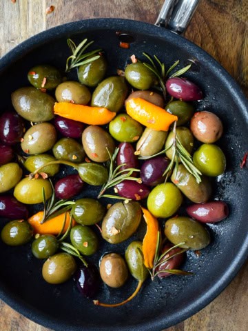 A skillet of warm olives with rosemary and clementine peels.