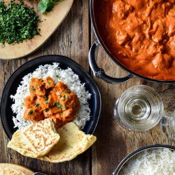 A pan of grilled chicken tikka masala and an individual portion is served on a bed of rice with naan.