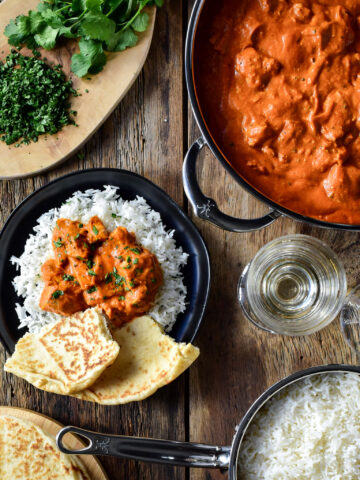 A pan of grilled chicken tikka masala and an individual portion is served on a bed of rice with naan.