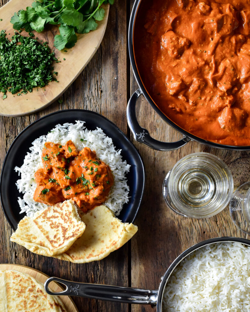 A pan of grilled chicken tikka masala and an individual portion is served on a bed of rice with naan. 