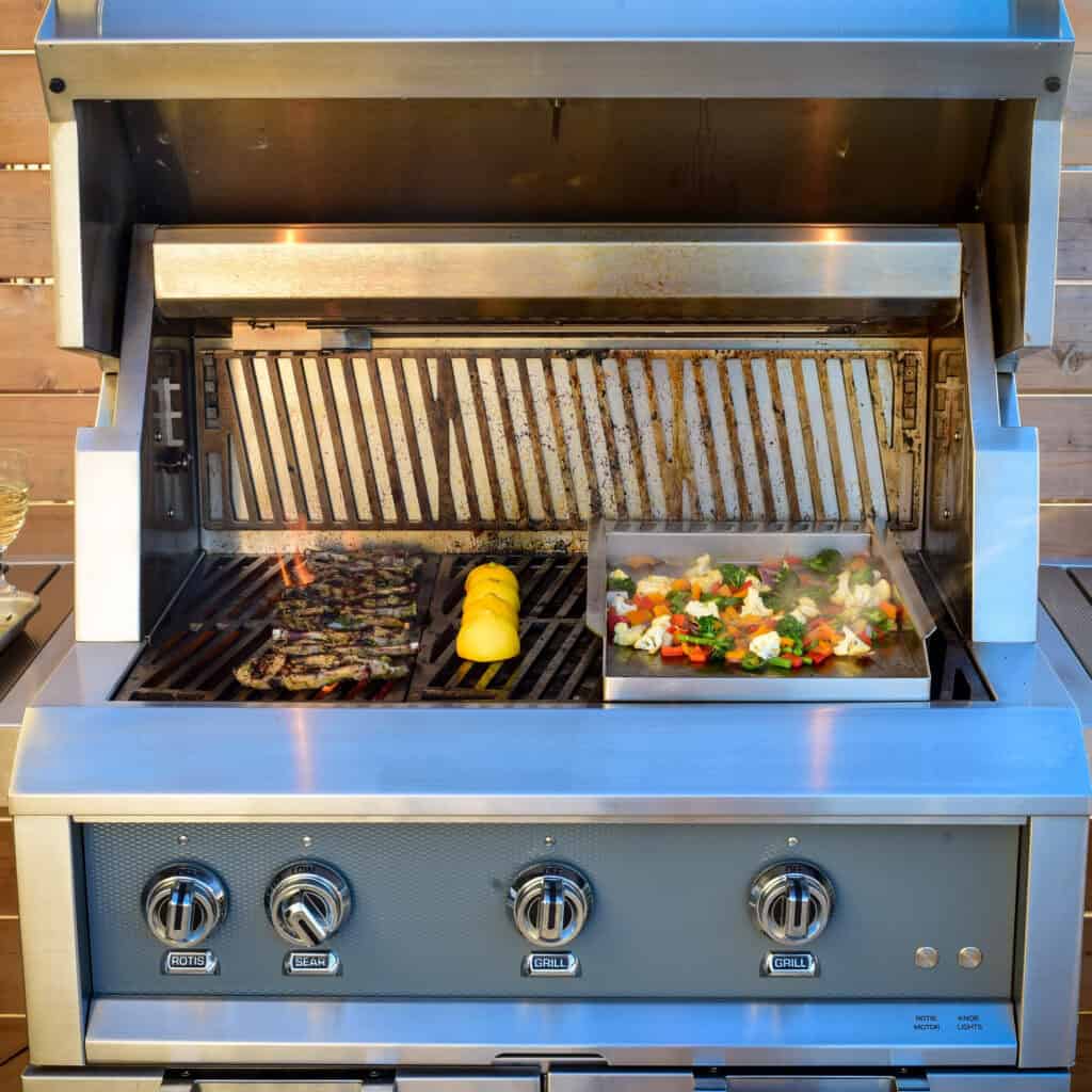 An open grill with lamp chops, lemons and vegetable being cooked. 