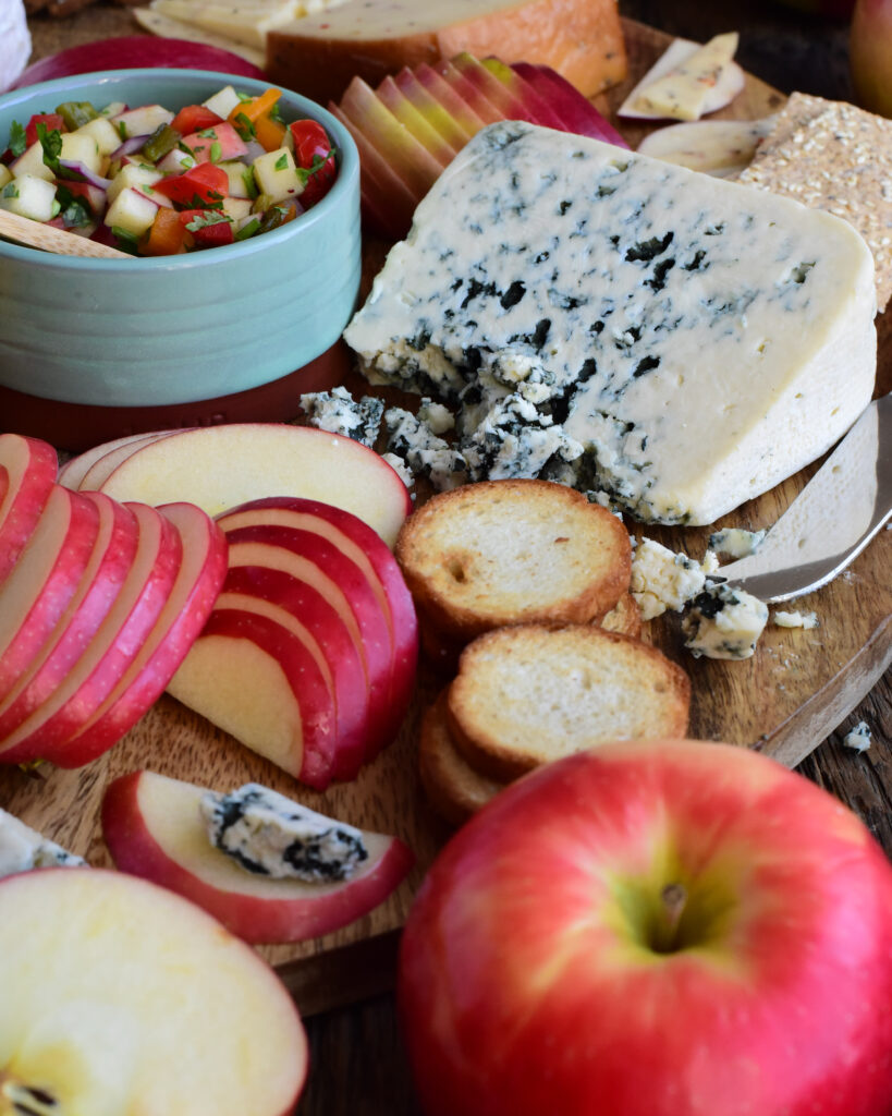 A close up image of an apple and cheese board, featuring a wedge of blue chees and semi-circles of apples.