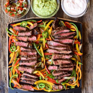 Slices of steak are laid on top of cooked peppers and onions on the Ooni grizzler plate. Served with three sauces.