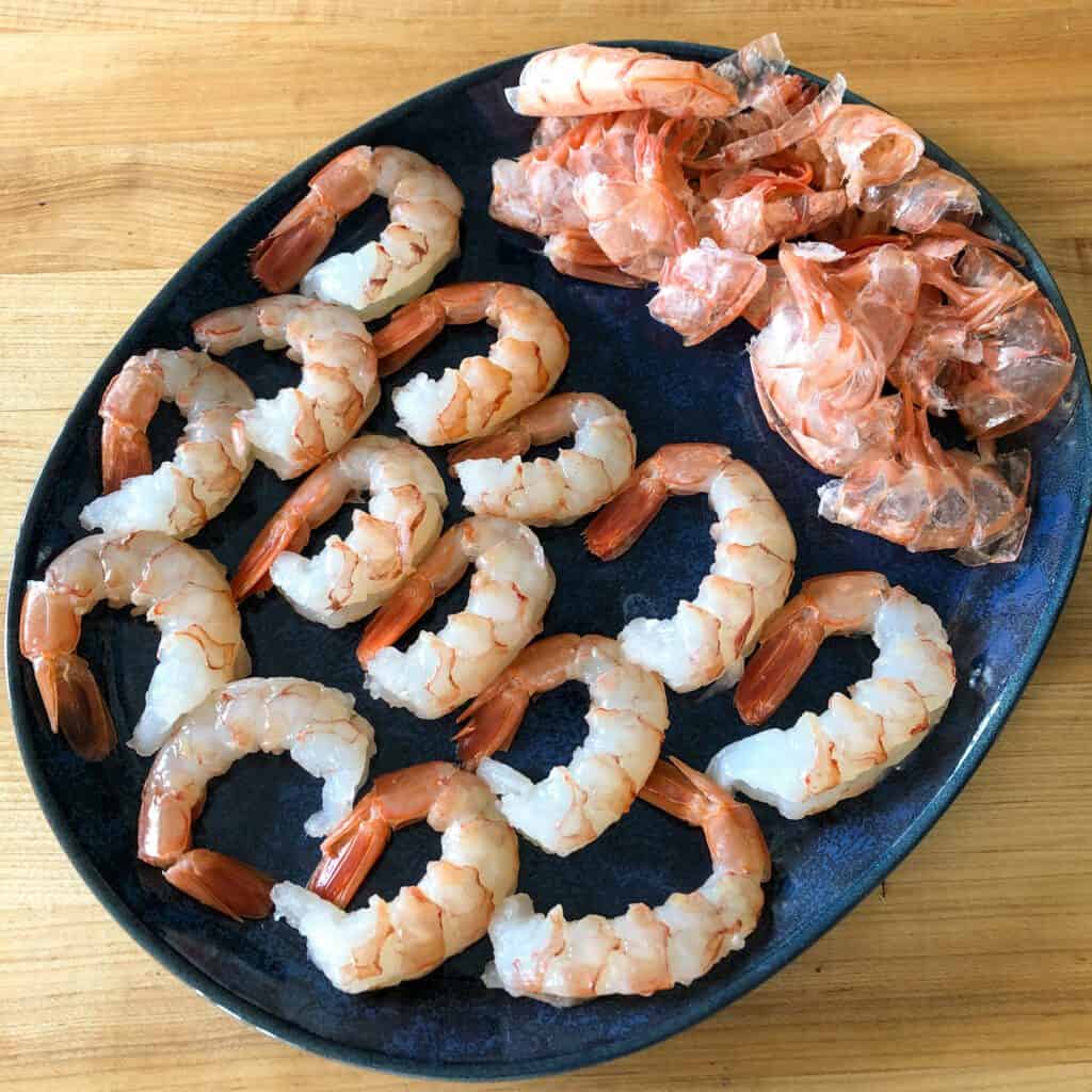 A blue oval plate of shrimp, shells removed and tails remain on.