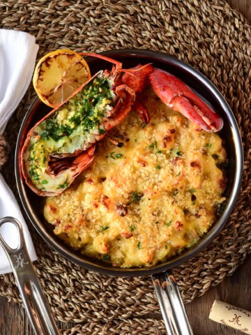 A small skillet with half a lobster sitting on a small skillet with mac and cheese.