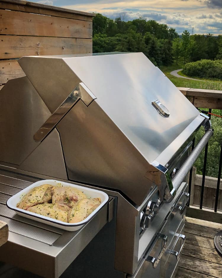 A tray with four marinated chicken breasts on the side table beside a grill.