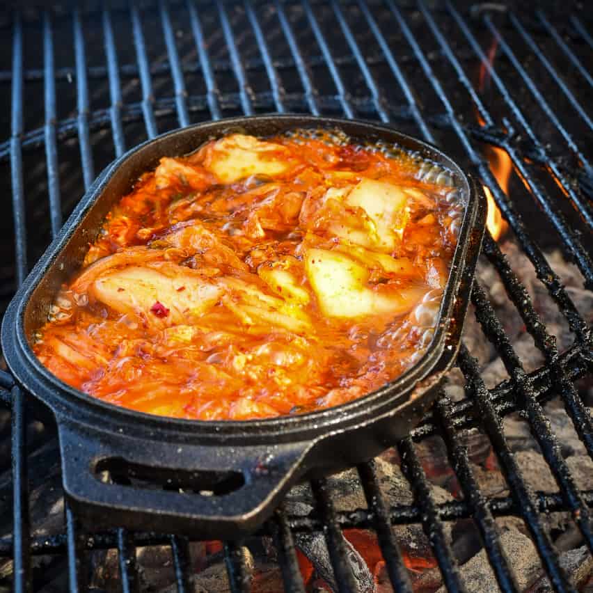 A cast-iron skillet on a hot grill caramelizing kimchi