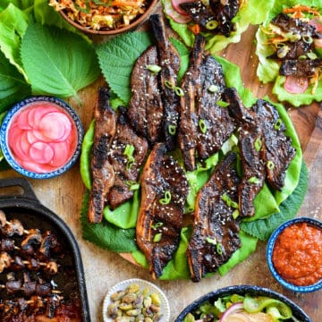 A Korean-Style Barbecue Beef Short Rib Lettuce Wraps spread on a board with coleslaw, salad, grilled mushrooms and kimchi.